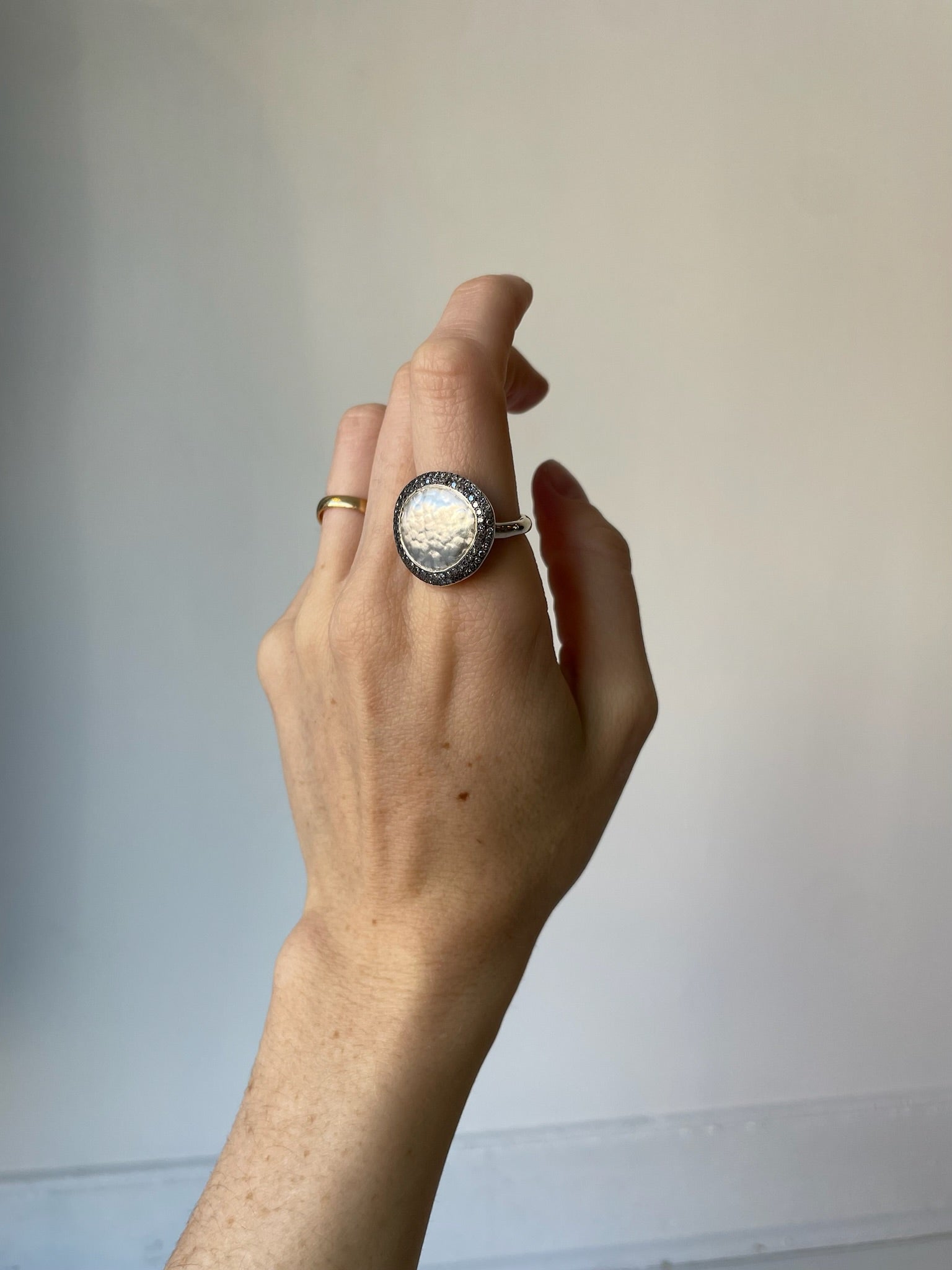 Hand wearing a large ring with a scenic design against a plain background organic and cool
