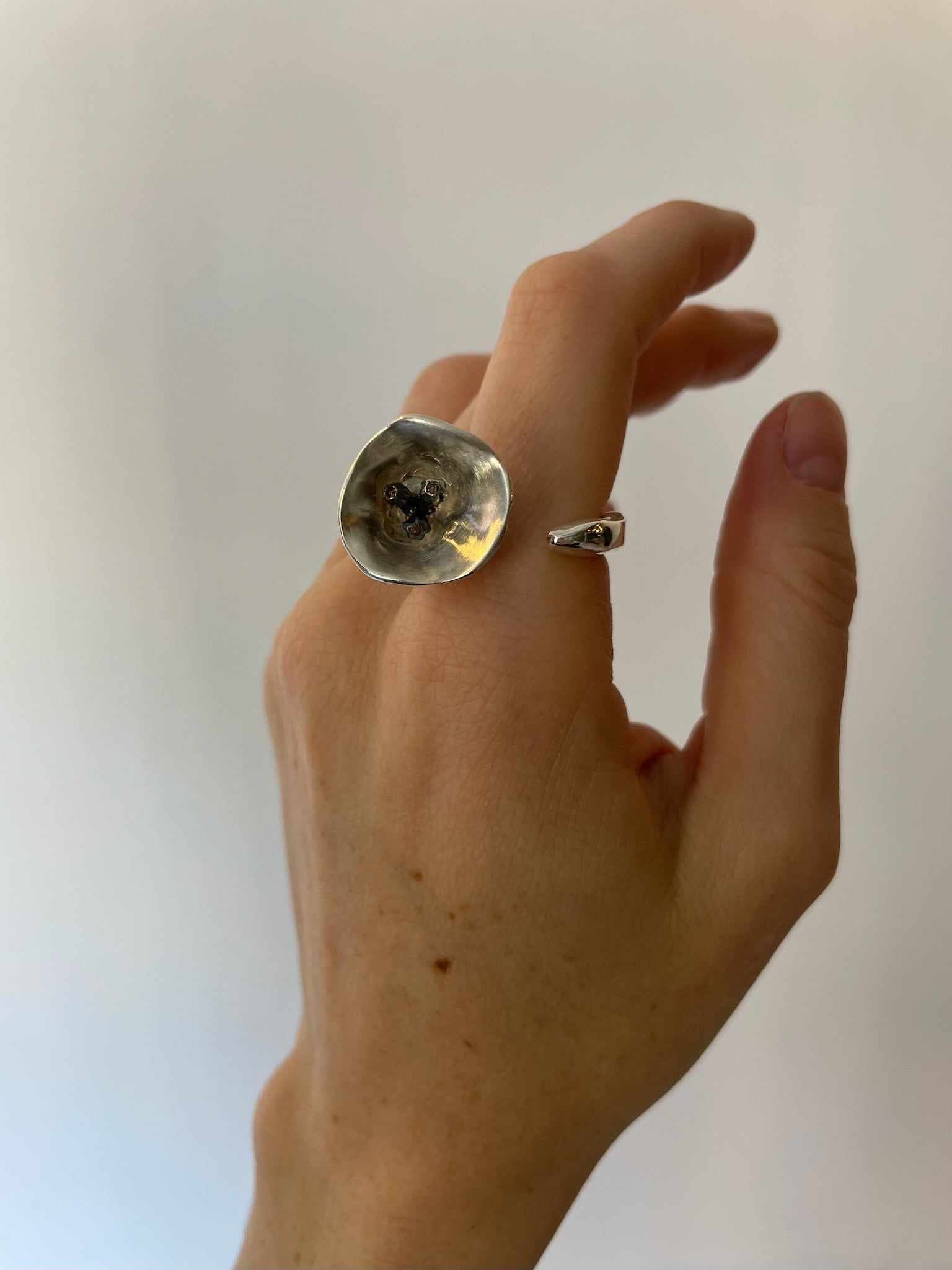 Hand wearing a large silver ring with a dark stone on a plain background