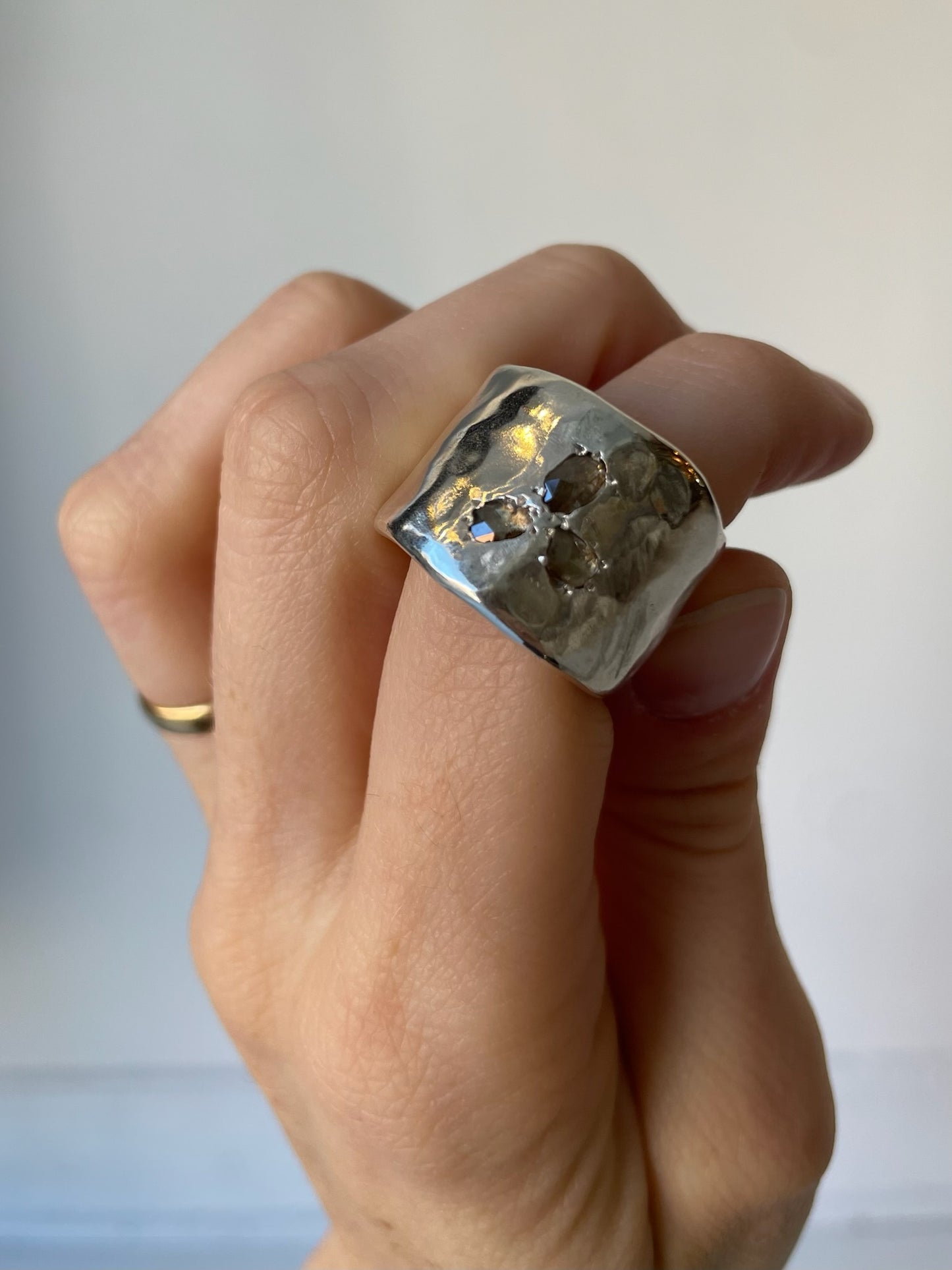 Hand wearing a large silver ring with a textured surface on a neutral background