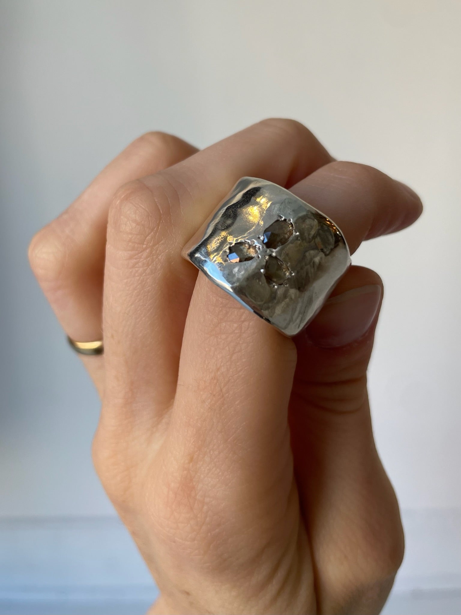 Hand wearing a large silver ring with a textured surface on a neutral background